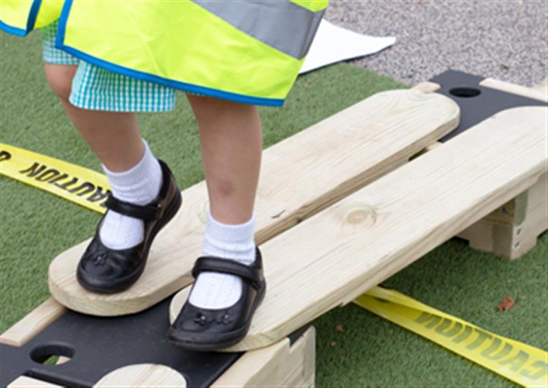 Zoomed in image of a child standing on two button planks, evaluating the space around her.